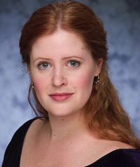 A woman with red hair and light eyes smiles at the camera.