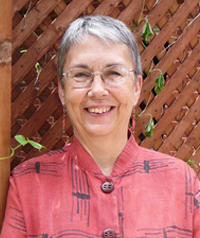 An older woman in a red button up shirt smiles at the camera.