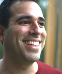 A man with a red shirt laughs while looking away from the camera