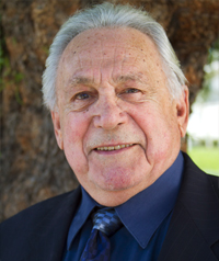 An older man in a suit smiles at the camera.