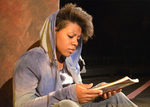 An actor reading a paper while sitting and leaning against a wall