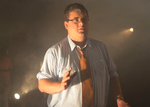 an actor stands alone with his right hand in front of his torso on an ash-ridden set