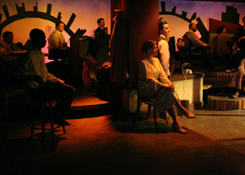 dimly lit stage, there are actors sitting and looking out