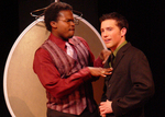 an actor looking into the audience while another actor has his fingertips on the other's chest
