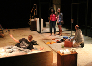 actors lounging around a messy room, two are standing and looking around