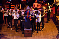 actor standing in center with arms out, all other actors are holding a rope in a circle formation