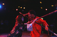 two actors in a close duel with swords, glaring at one another