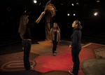 actors standing in a triangle formation, one is holding an object up and the other two are looking up at it