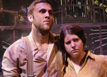 two actors standing, one is nearly leaning their head on the other's shoulder