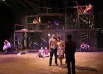 two actors confronting a black silhouette, there are other actors in the background