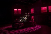 dimly lit stage with a group of male actors pointing while seated in a car