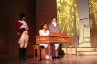 actor sitting at a desk, there are two actors guarding her