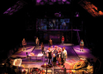 actors in the front center of the stage joining hands in a triangle formation, there are also actors standing in the main part of the stage