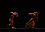 two dancers in striking a pose in a squat position, their right arms are reaching toward their left shoulder