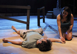 an actor sprawled on the ground with another actor on their knees, holding their hand