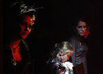 an actor looking to the right, in the background there is a child and another actor, a white light is shining on the child