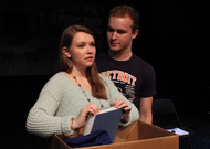 actor going through items in a box, another actor is behind her gazing at her