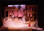 two actors speaking on the right side of the stage while someone stands in the distance