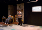 an actor standing next to another actor sitting in a reclining chair