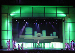actor centered on stage with other actors on the left and right of the stage