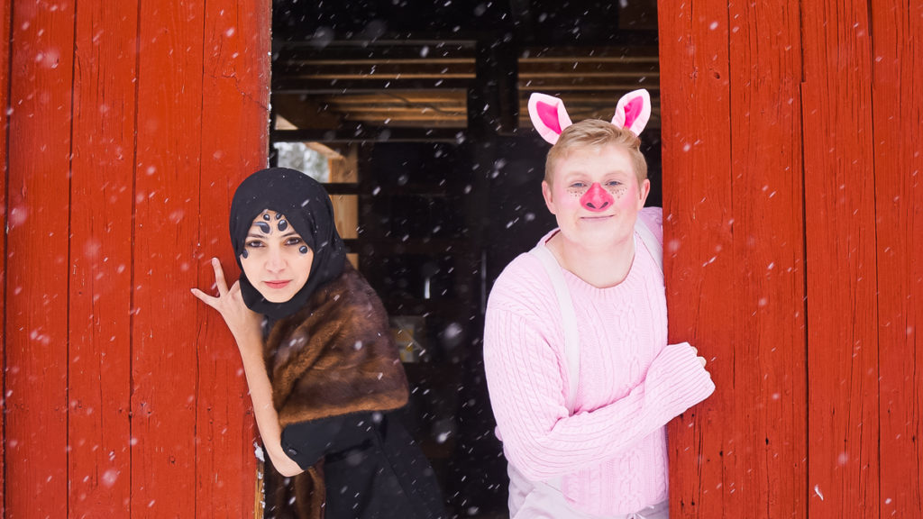A picture of two actors in costumes peeking out from behind barn doors.