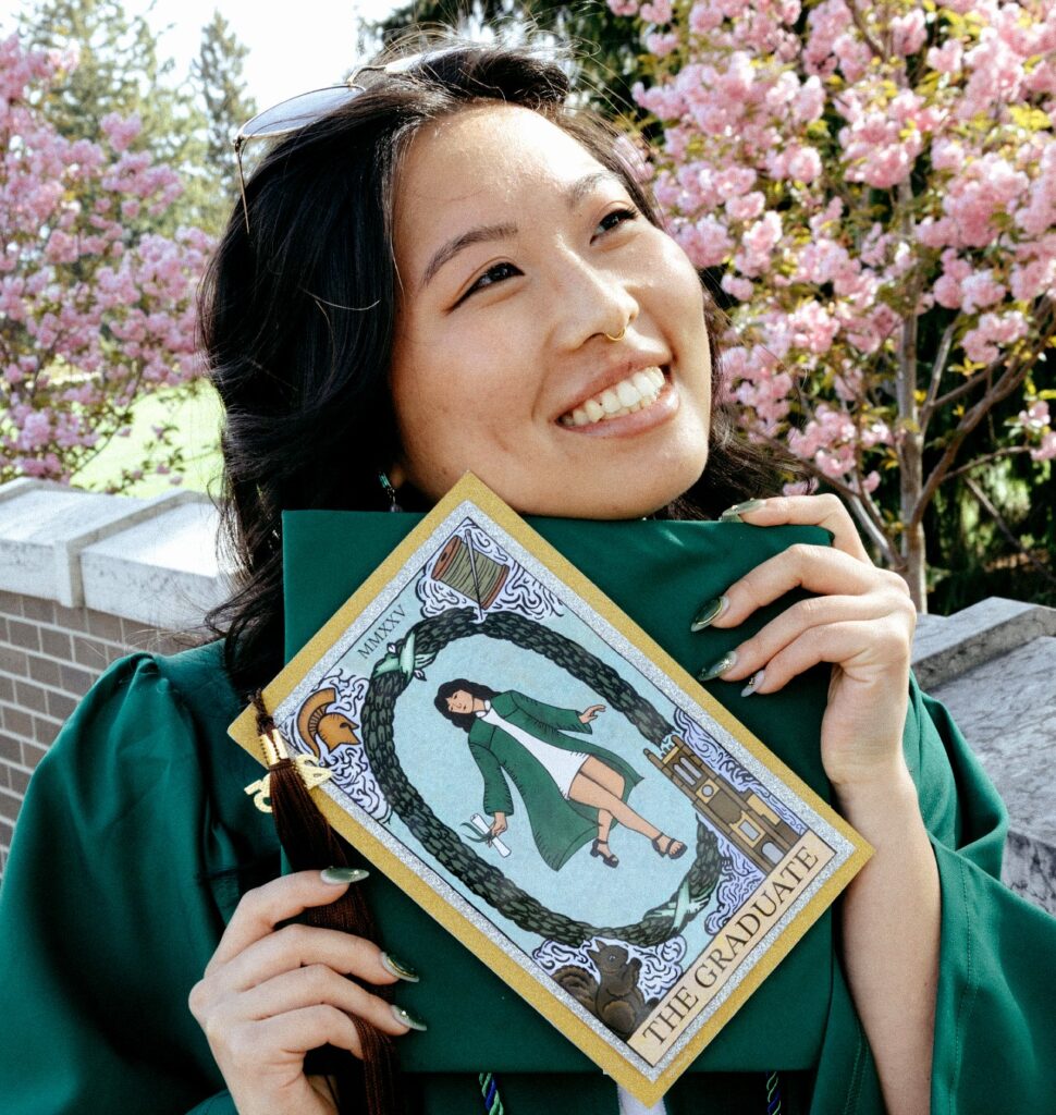 Photo of a woman wearing a green graduation robe and holding a green graduation cap and a picture that shows a woman in the center wearing a graduation robe and in each of the four corners are images of a squirrel, the MSU Spartan logo, Beaumont Tower, and a needle and thread. At the bottom of this picture, it says: "The Graduate."