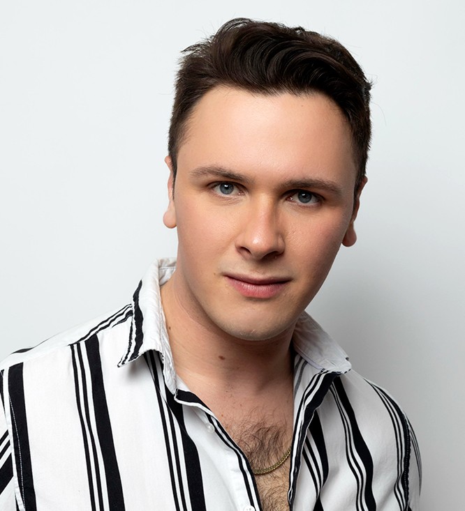 A close-up headshot of a person with short brown hair wearing a black-and-white striped shirt, looking directly at the camera with a neutral expression.