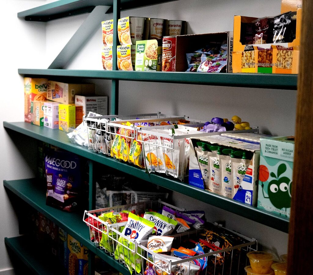 Shelves in a small food pantry are stocked with a variety of packaged items. 