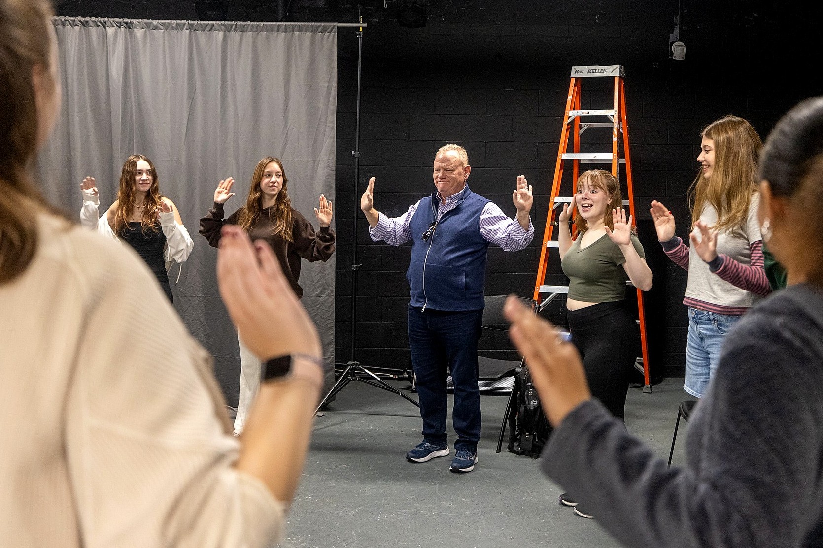  A group of people standing in a circle with both their hands raised.