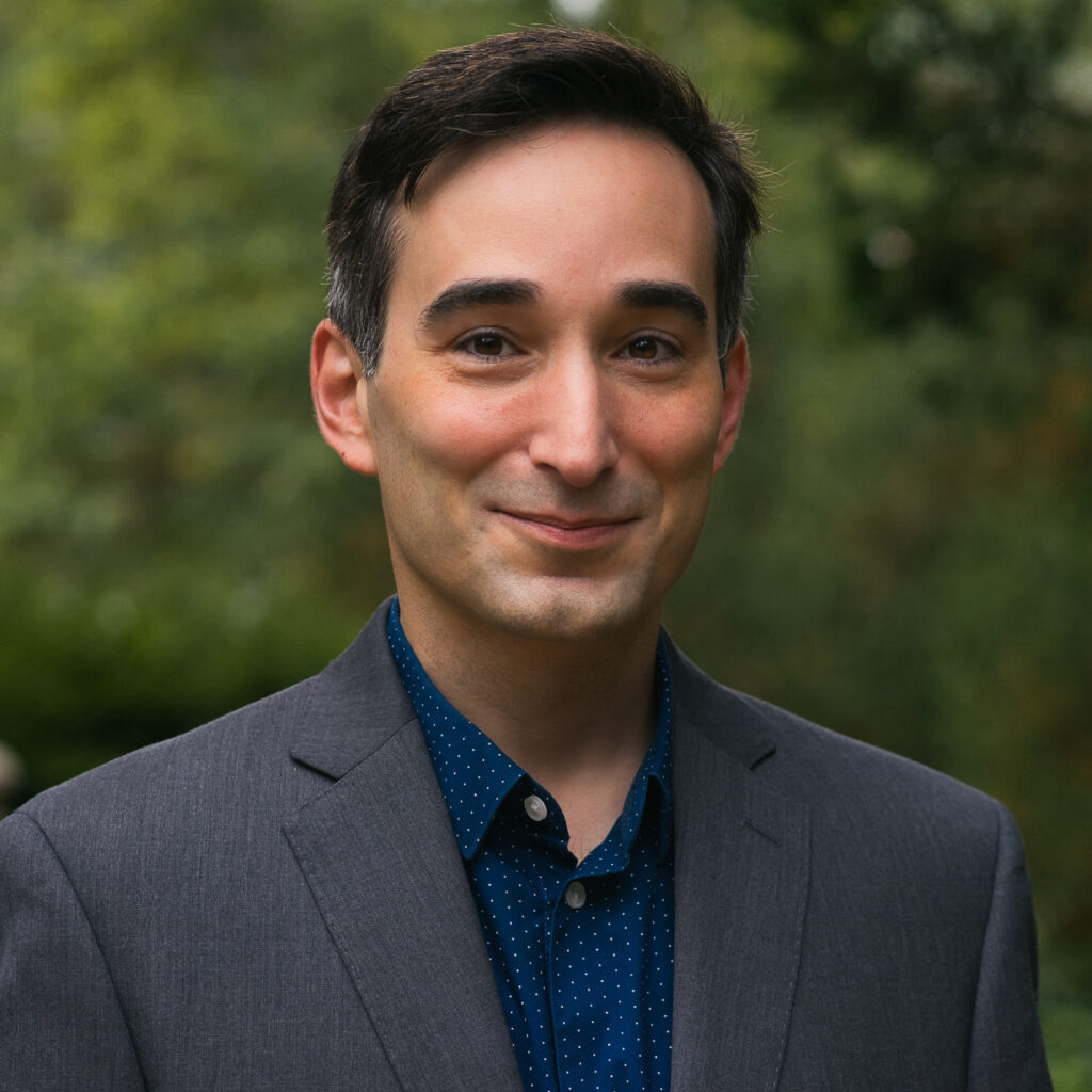 A head-and-shoulders portrait of a person with short dark hair wearing a blazer and collared shirt.