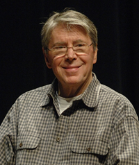An older man with glasses smiles away from the camera.
