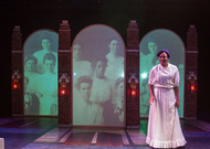 actor standing on the right of the stage, there is an old photo of a class projected behind her