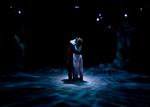 two actors embracing in the center of the stage with a dim blue light shining on them