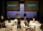actors standing around the stage, the background has two words displayed on the left and right, reading "destroy" and "destry" respectively