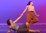 dancer laying on their side holding another dancer's hand who is standing