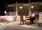 actor sitting at the dining table while another actor walks toward them from the other side of the stage