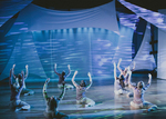 dancers sitting on the ground with both arms in the air, a projection of water is in the background