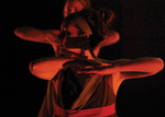 two dancers illuminated by a dim red light, their arms held parallel and against their chest