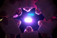 girls holding books on top of camera, forming a circle with their faces peeking out