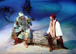 two actors sitting on a snowy log and talking