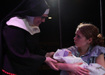a actor dressed as a nun holding the arm of a young actor holding a baby