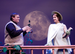 two actors conversing on a balcony with the moon in the background