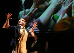 dancer with hands up like claws, an image of arms in projected in the background