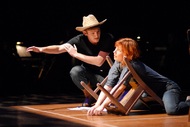 actor in a cowboy hat speaking to an actor who has fallen over a chair