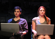 two actors sitting in two chairs side-by-side with laptops on their laps
