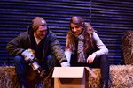 two actors sitting on hay bales and looking through a cardboard box