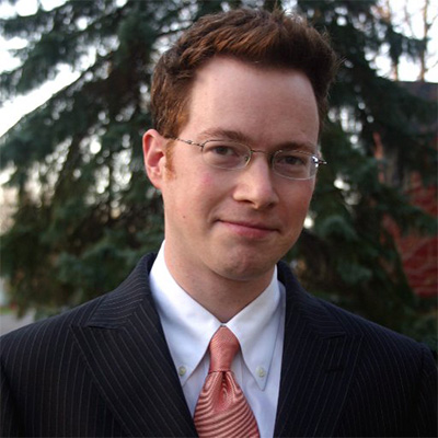 Man with red hair wearing glasses and a suit and tie.