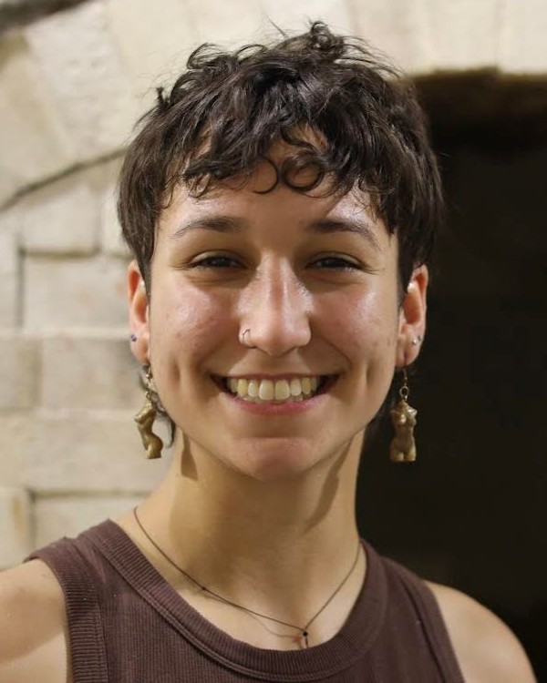 A picture of a person with brown hair and earrings smiling