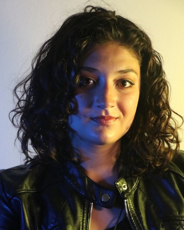 A picture of a person with wavy brown hair and a black leather jacket